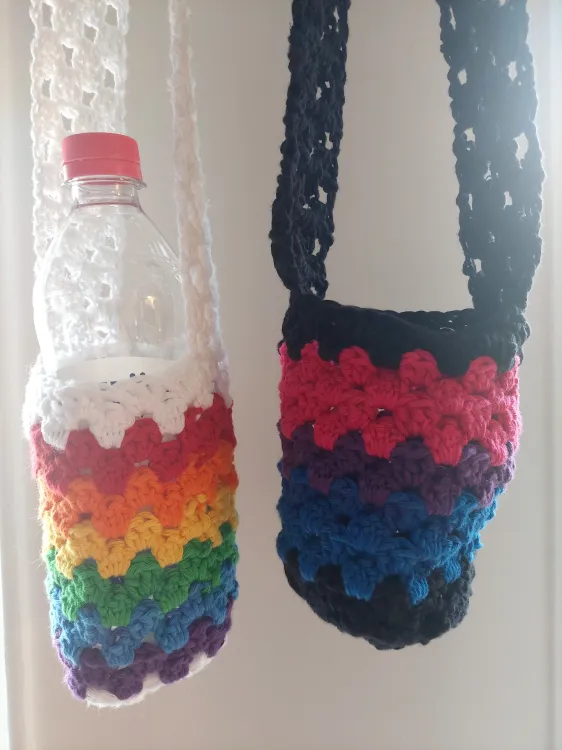 The same bottle holders hanging by their straps. The white one with rainbow colors is holding an empty plastic bottler. The black, blue, purple, and pink one is empty.
