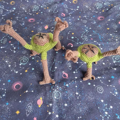Two posable crochet figure of Rocky from the novel Project Hail Mary by Andy Weir. Their bodies are brown, consisting of a brown five-sided disc with five legs. Each leg has three fingers. One figure has shorter legs. Both are holding two legs up.