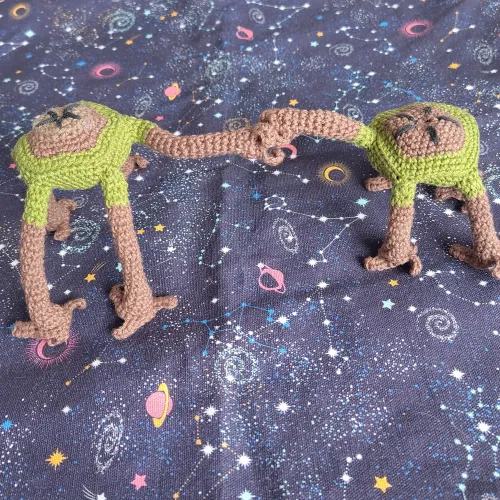 Two posable crochet figure of Rocky from the novel Project Hail Mary by Andy Weir. Their bodies are brown, consisting of a brown five-sided disc with five legs. Each leg has three fingers. One figure has shorter legs. They are bumping each others fists..