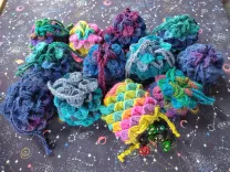 Twelve multicolor dragonscale dice bags on a starry tablecloth. Most are closed, but one is open and lying on its side with dice spilling out.