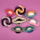 Crochet pins shaped like ringed planets, spiral galaxies, and accreting black holes in various LGBTQIA+ pride flag colors: lesbian, non-binary, aro-ace, asexual, agender, transgender, aromantic, men-loving-men.